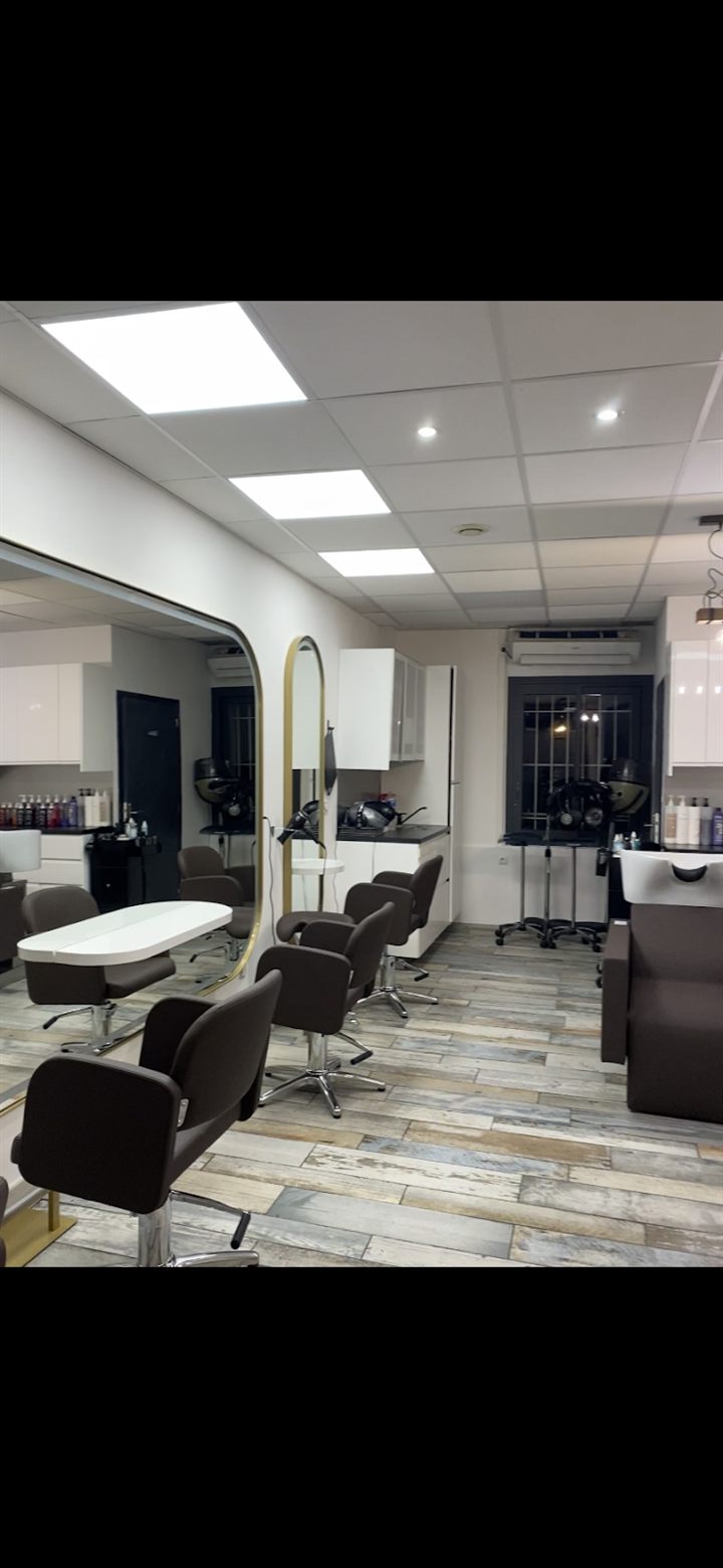 Intérieur du salon : fauteuils noirs, bac de lavage et parquet clair devant de grands miroirs